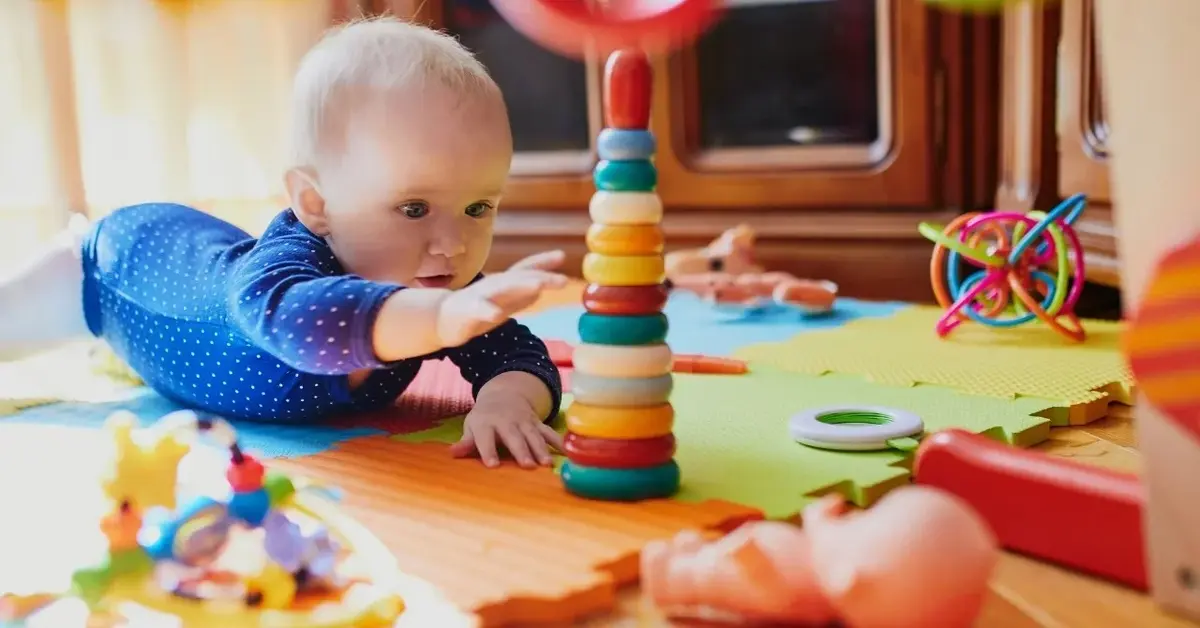 niemowlak sięga rączką do zabawki wieży z kolorowych okręgów leży na macie z zabawkami