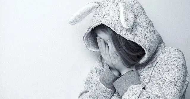 Dziecko w smutnej pozie, zakrywa dłońmi twarz, ubrane w onesie królika, czarno białe zdjęcie