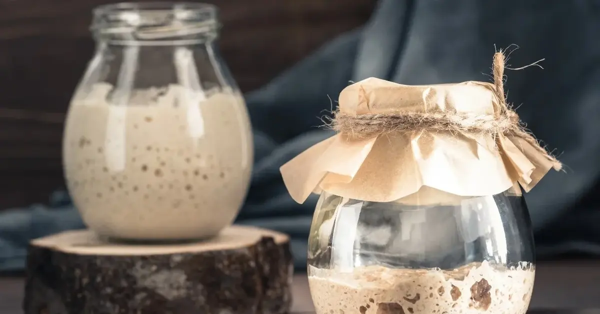 Dwa słoiki z zakwasem na wielkanocny żurek, jeden bez przykrycia, drugi zasłonięty szmatką z gumką recepturką.