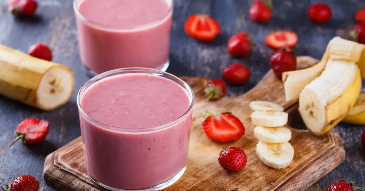 Koktajl owocowy z kefirem w szklance, obok truskawki i banany