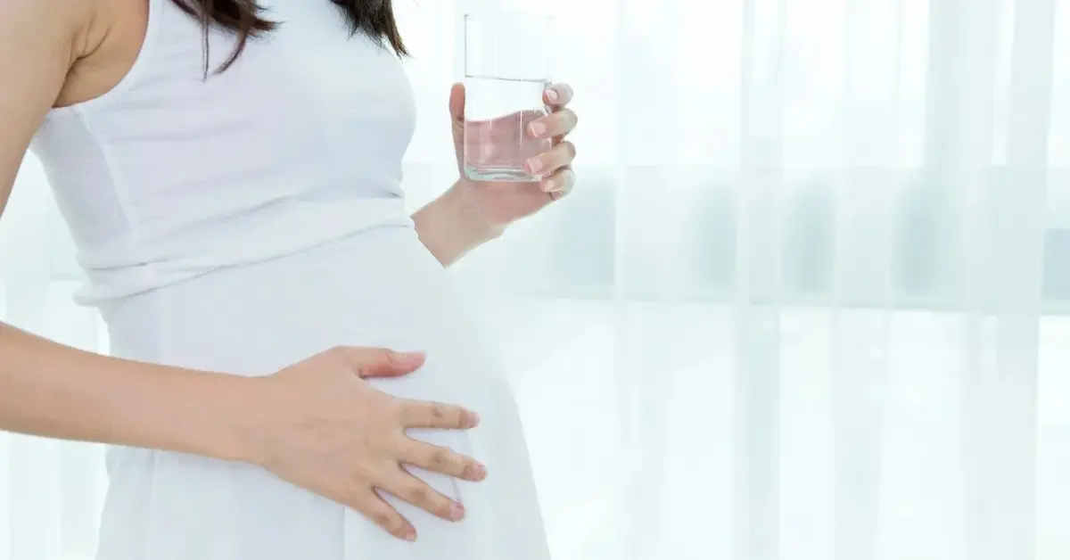 Kobieta w ciąży trzymające szklanke wody w rękach 