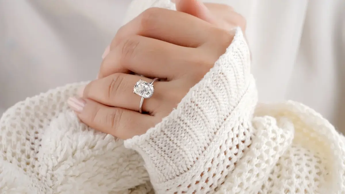 pierścionek zaręczynowy na palcu kobiety w białym swetrze 