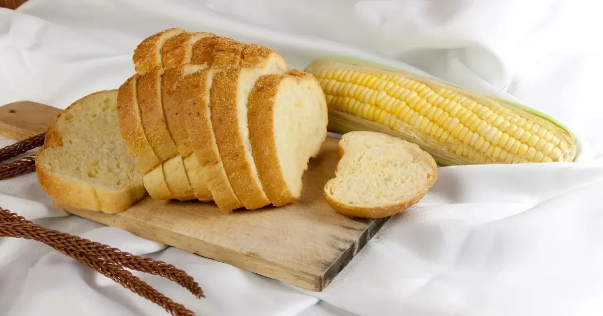 Kromki chleba kukurydzianego na drewnianej desce. Obok kolba kukurydzy