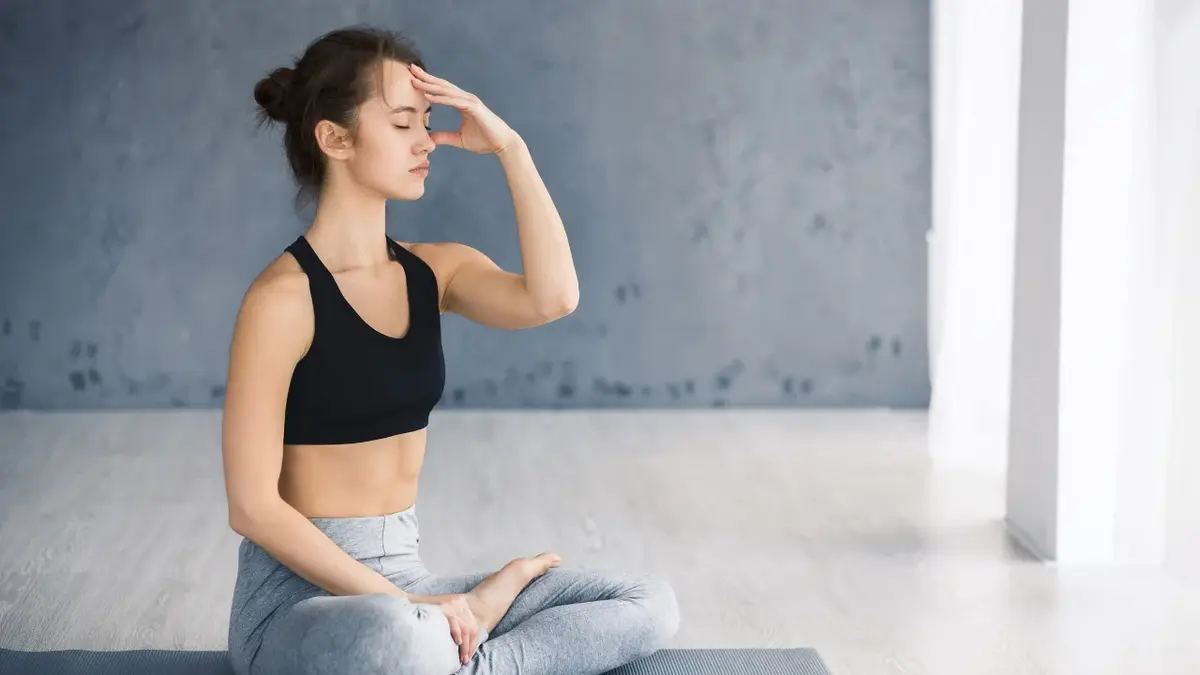 Kobieta w pozycji do medytacji na macie do ćwiczeń przykładająca dłoń do czoła
