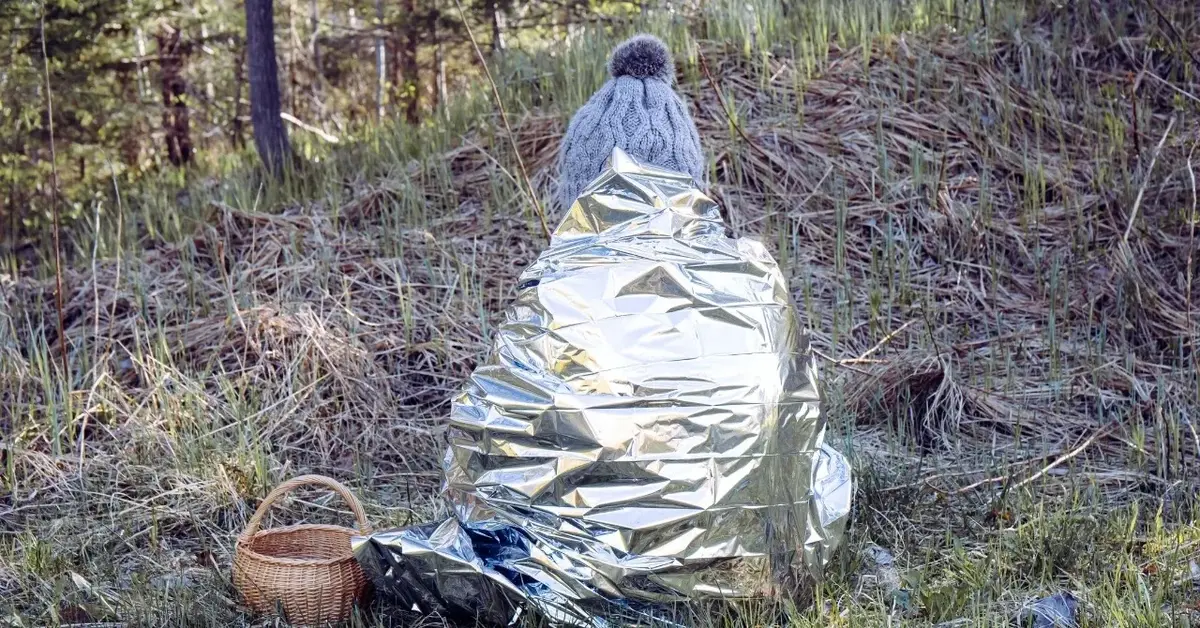 Osoba w lesie owinięta srebrną termiczną płachtą