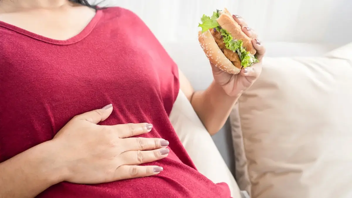 Kobieta z wzdętym brzuchem trzymająca w ręce hamburgera