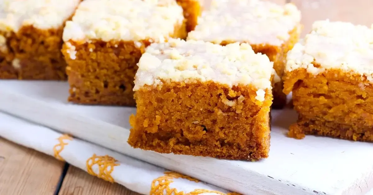 Ciasto dyniowe pokrojone na kwadratowe kawałki leży na białej serwetce z żółtym haftem