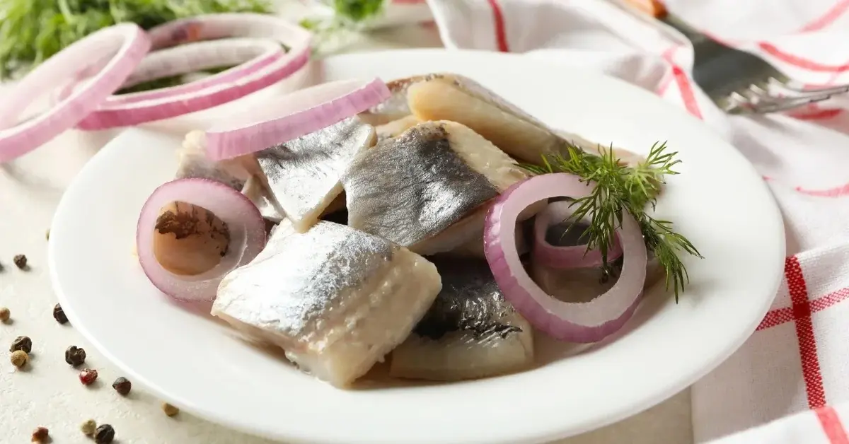 Śledzie z rodzynkami i cebulą w białym głębokim talerzu