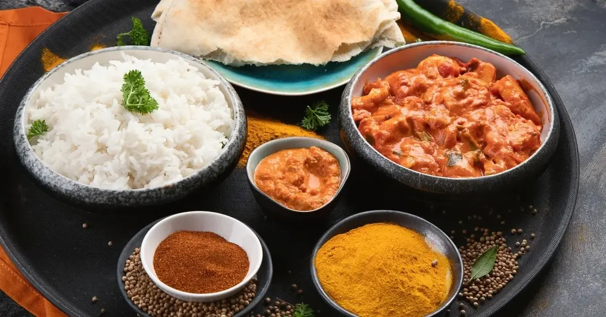 Kurczak tikka masala z ryżem na tacy z przyprawami w miseczkach, chlebkiem pita