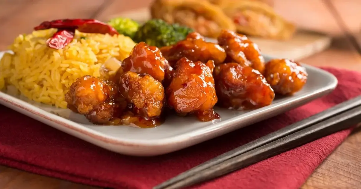 Kurczak Generała Tso z ryżem na talerzu. Obok pałeczki