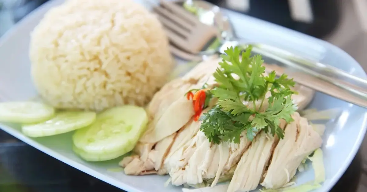Pierś z kurczaka gotowana na parze na talerzu z ryżem i świeżymi ogórkami