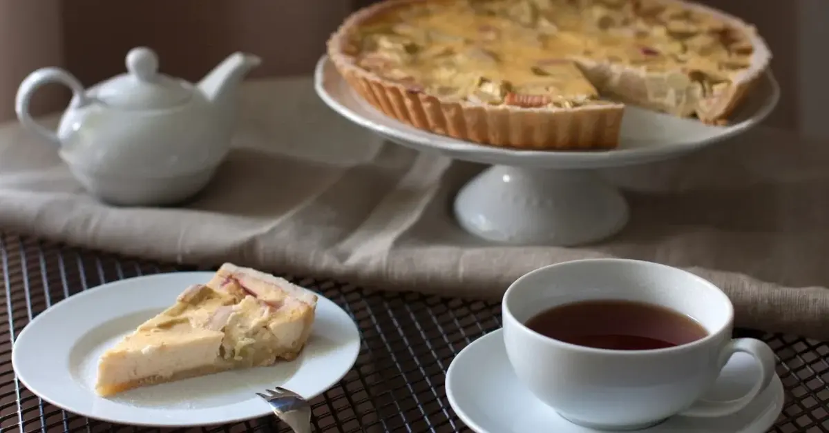 Ciasto z barbarem i budyniem na paterze, obok porcja ciasta na talerzyku deserowym i filiżanka kawy