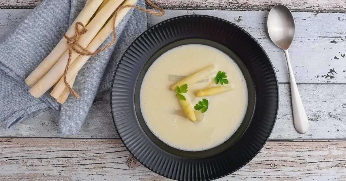 Zupa krem z białych szparagów w miseczce, obok białe szparagi