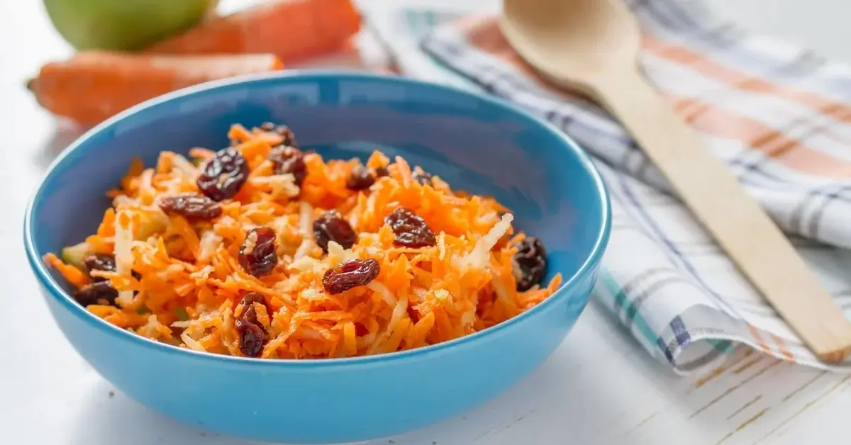 surówka z marchewki i jabłka w niebieskiej miseczce. Obok tarka do warzyw