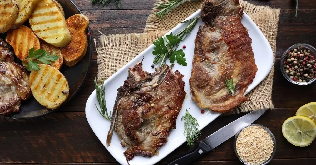 Schabowy bez panierki na białym półmisku. Obok grillowane warzywa i dodatki