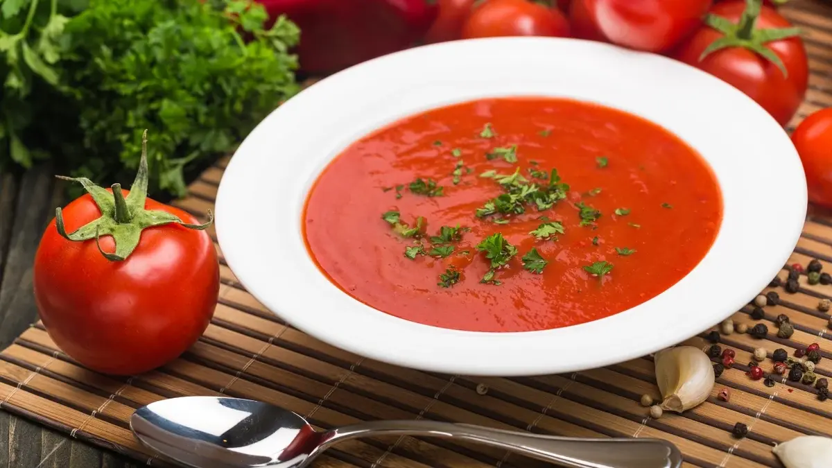 W białym dużym talerzu zupa pomidorowa gotowana na rosole, obok pomidor