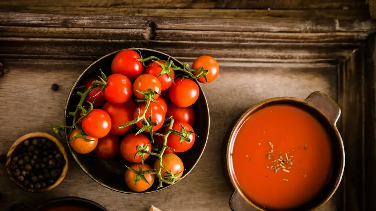 W miseczce zupa pomidorowa, obok na talerzu pomidorki koktajlowe w kiściach