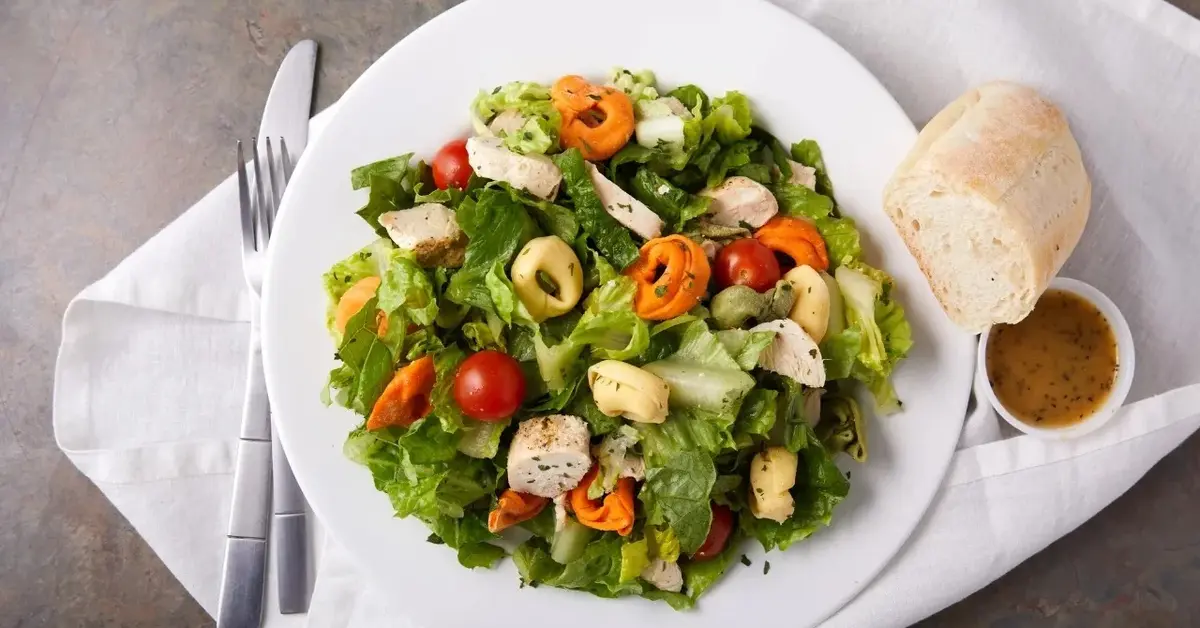 Sałatka z tortellini z rukolą, oliwkami i pomidorkami na białym talerzu