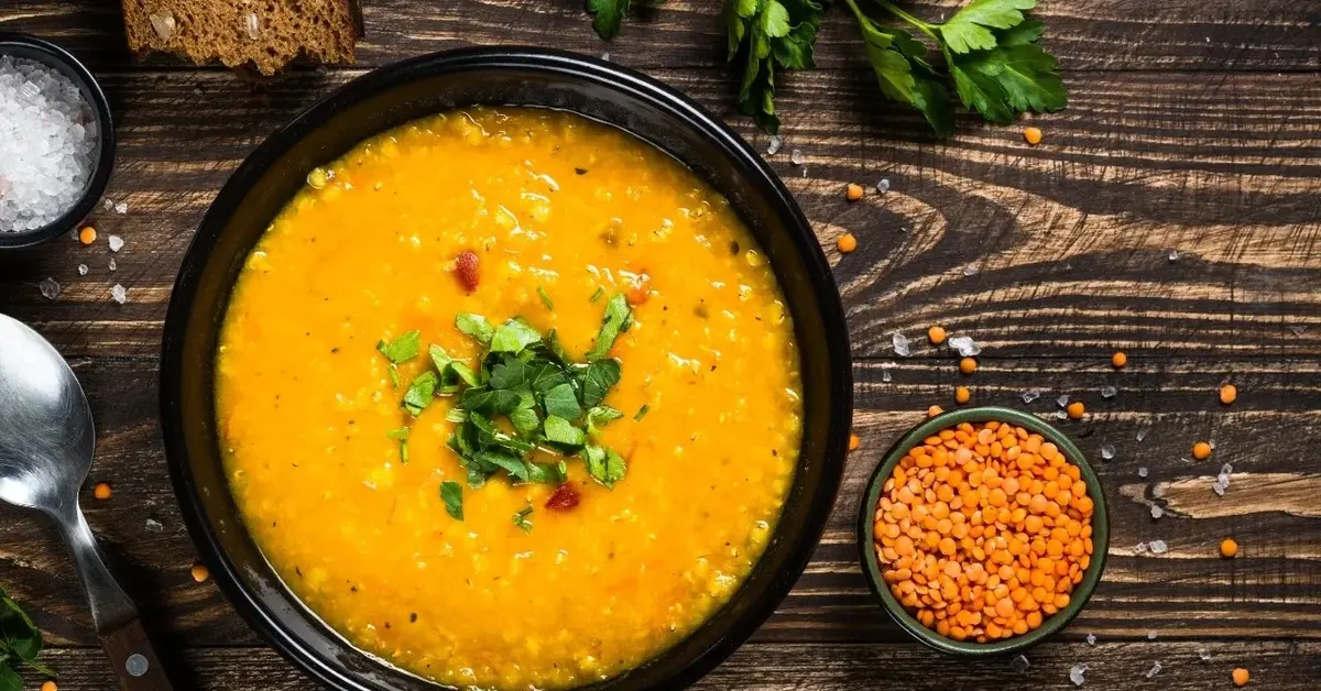 Zupa dyniowo-soczewicowa w czarnej miseczce, obok mała miseczka z czerwoną soczewicą