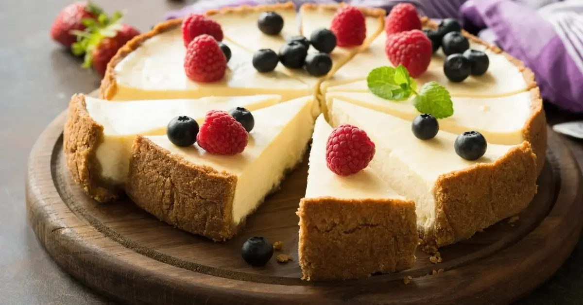 Sernik z owocami pokrojony na porcje na drewnianej desce