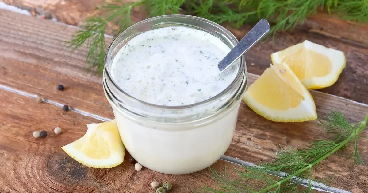 Sos koperkowy w szklanym słoiczku, obok pęczek koperku i ćwiartki cytryny