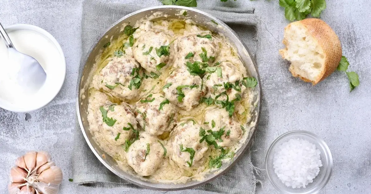 Pulpety w sosie chrzanowym w garnku, obok dodatki: kawałek chleba, miseczka z sosem i solą