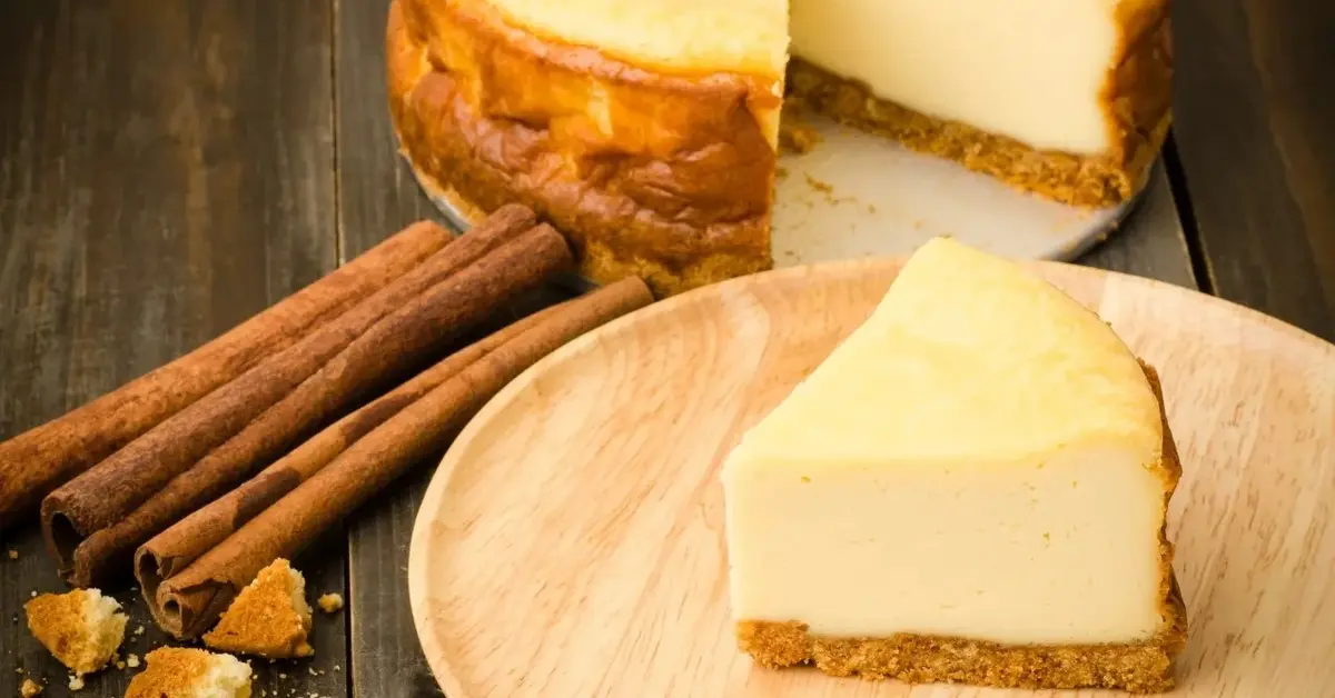 Sernik z serków homogenizowanych w tle, na pierwszym planie talerzyk z porcją sernika