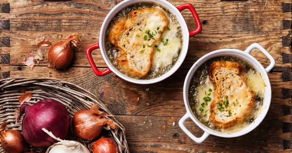 Zupa cebulowa w dwóch małych miseczkach z uszkami z  zapieczonymi grzankami z serem na wierzchu