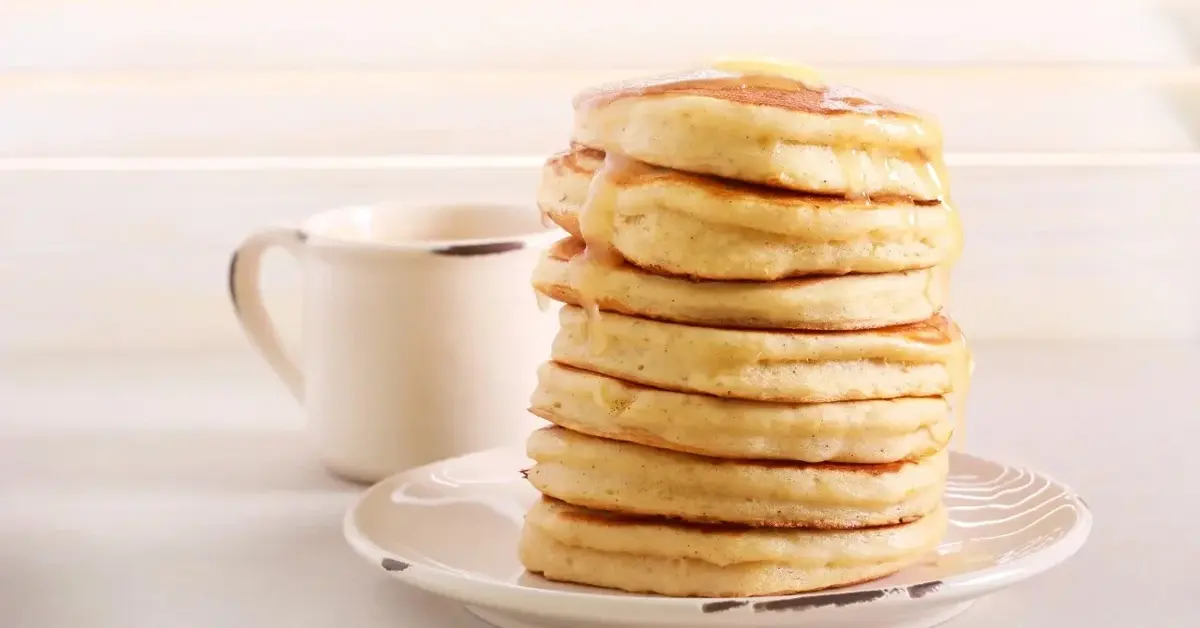 Puszyste racuchy na sodzie ułożone na sobie w wieżyczkę, obok dzbanuszek z sosem