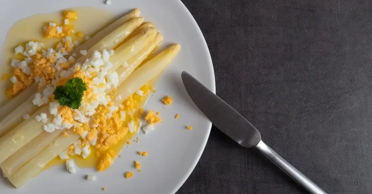 Szparagi z jajkami w sosie maślanym na białym talerzu