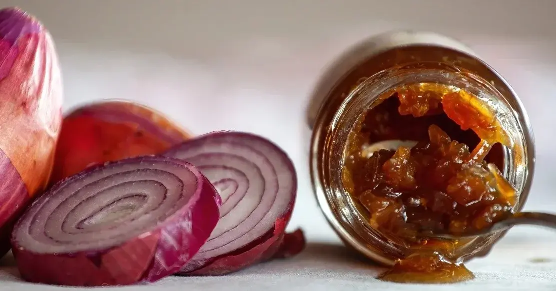 Konfitura z czerwonej cebuli w słoiczku, obok czerwone cebule