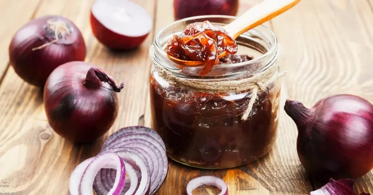 Konfitura z czerwonej cebuli w słoiczku, obok czerwone cebule