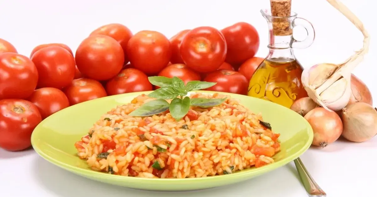 Risotto z pomidorami na talerzu, w tle pomidory, oliwa i czosnek