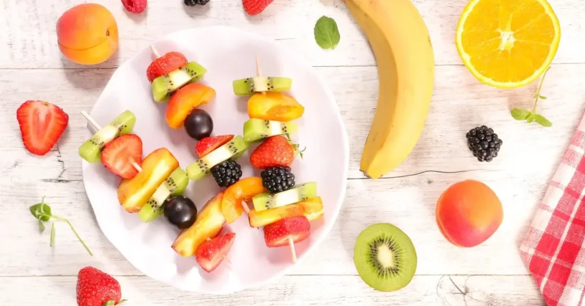 Szaszłyki owocowe z winogron, bananów i truskawek na talerzyku