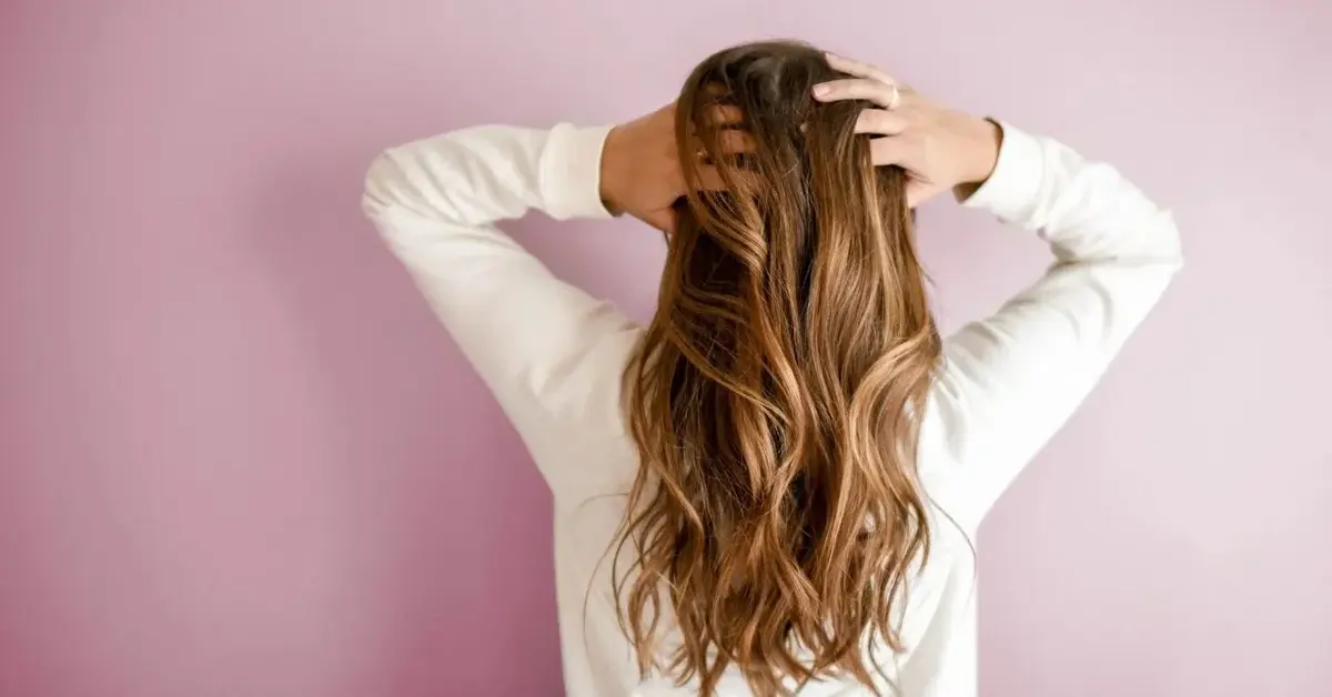 Modelka z długimi brązowymi włosami na różowym tle