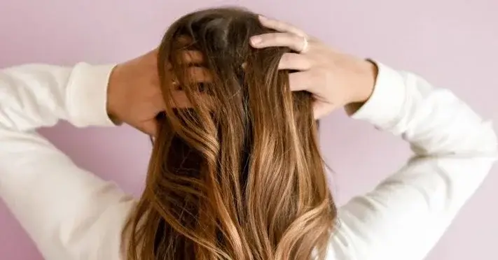 Modelka z długimi brązowymi włosami na różowym tle