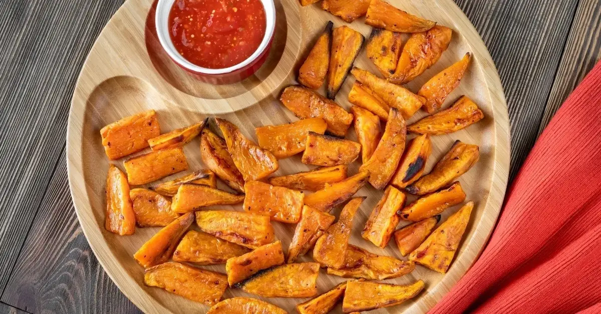 Pieczone bataty w kawałkach na drewnianej desce z sosem