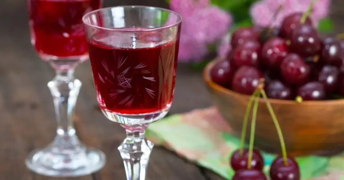 Nalewka z wiśni zasypanych cukrem w kieliszku, obok miseczka z wiśniami