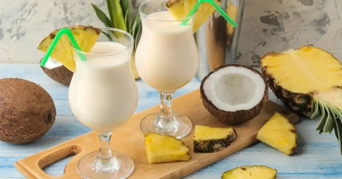 Pina Colada w wysokich kieliszkach, obok połówki kokosa i ananasa
