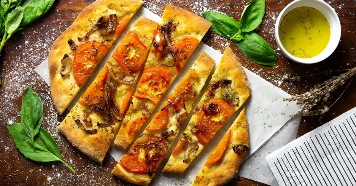 Focaccia z pomidorami, obok miseczka z oliwą i świeża bazylia