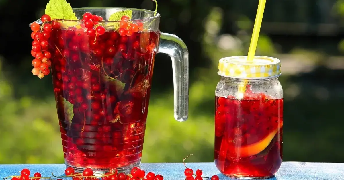 Sok z czerwonej porzeczki w dzbanku, obok szklanka z sokiem