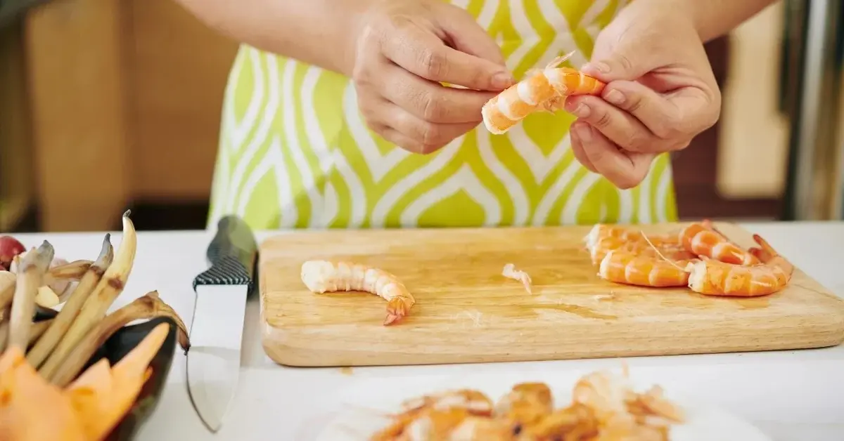 Ręce kobiety obierającej krewetki przy blacie kuchennym