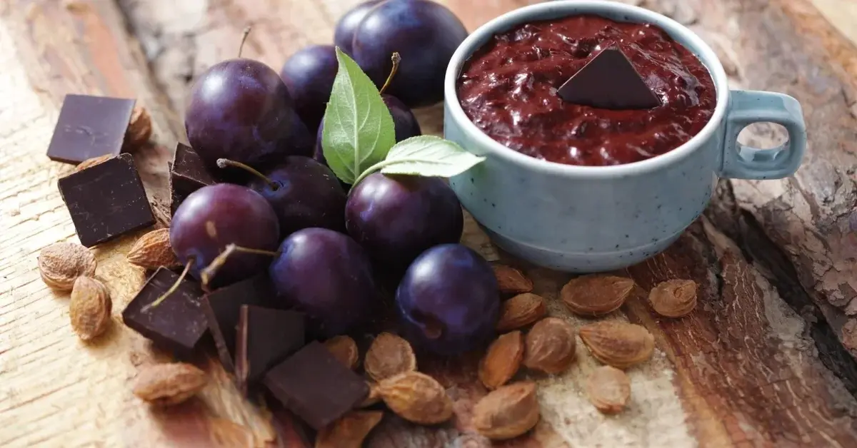 Powidła śliwkowe z czekoladą w miseczce, obok czekolada i świeże śliwki