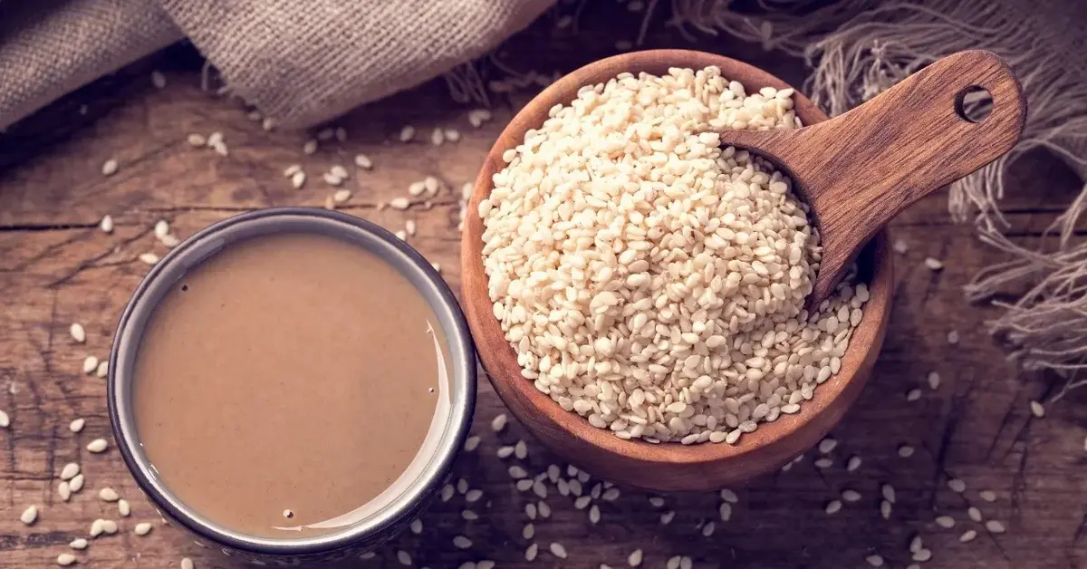 Pasta tahini w miseczce, obok miseczka z ziarnami sezamu