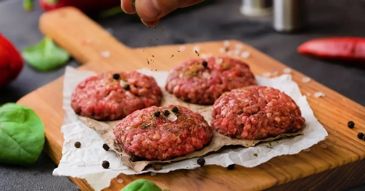 Surowe mięso przygotowane w formie kotletów na drewnianej desce