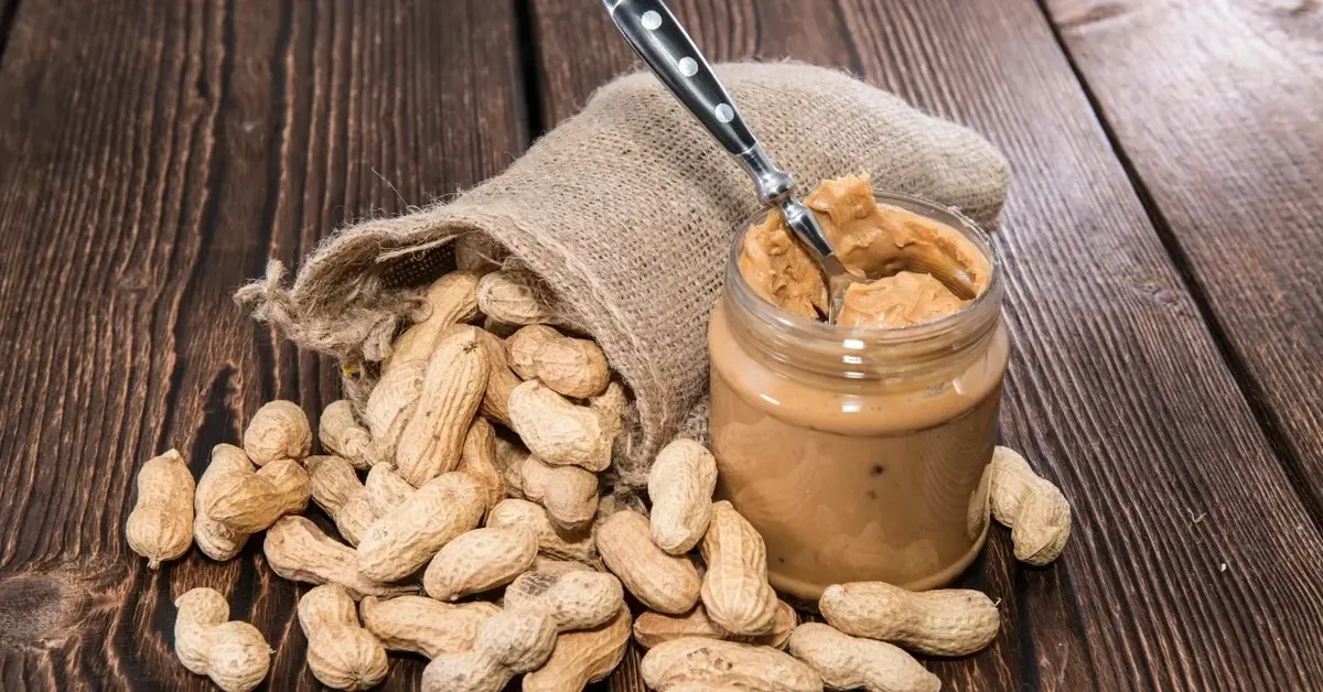Masło orzechowe w sloiku, obok orzeszki ziemne