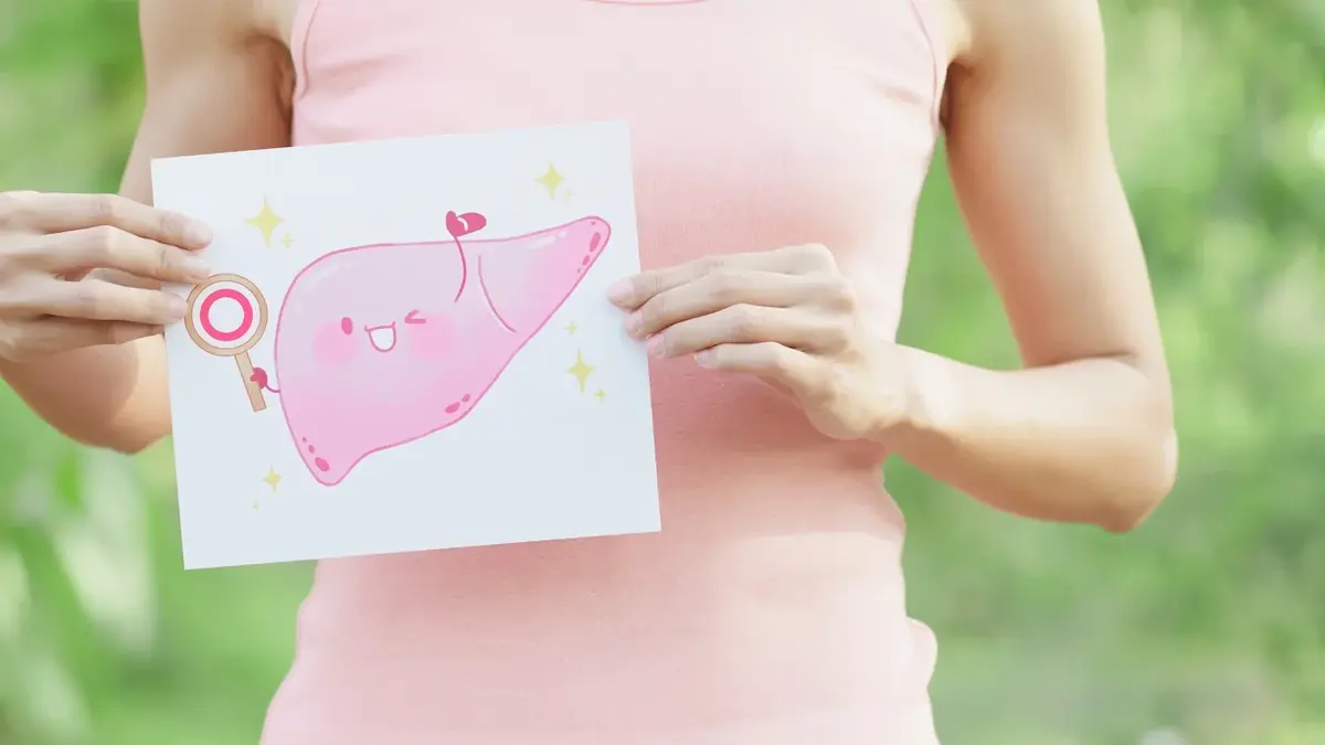 Kobieta w różowej koszulce trzyma przed sobą kartkę z narysowaną wątrobą