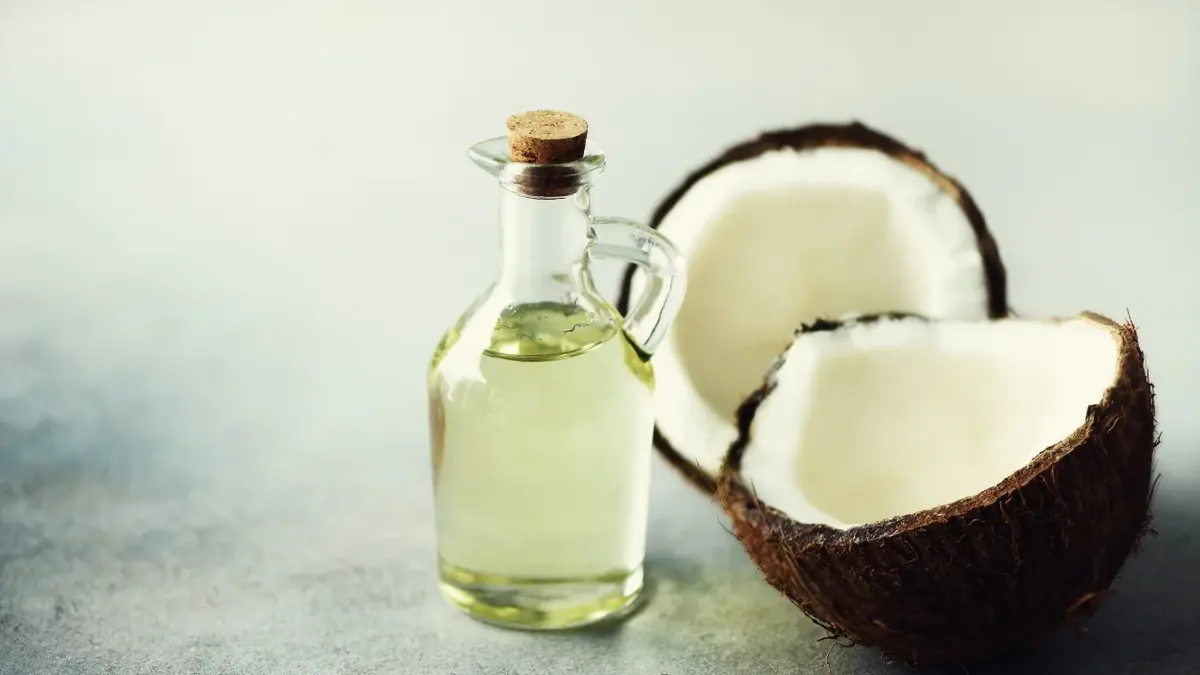 Olej kokosowy w buteleczce, obok łupinki świeżego kokosa