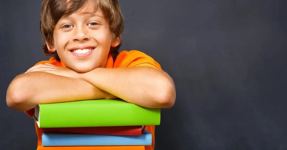 Rudy chłopiec oparty na kolorowych zeszytach