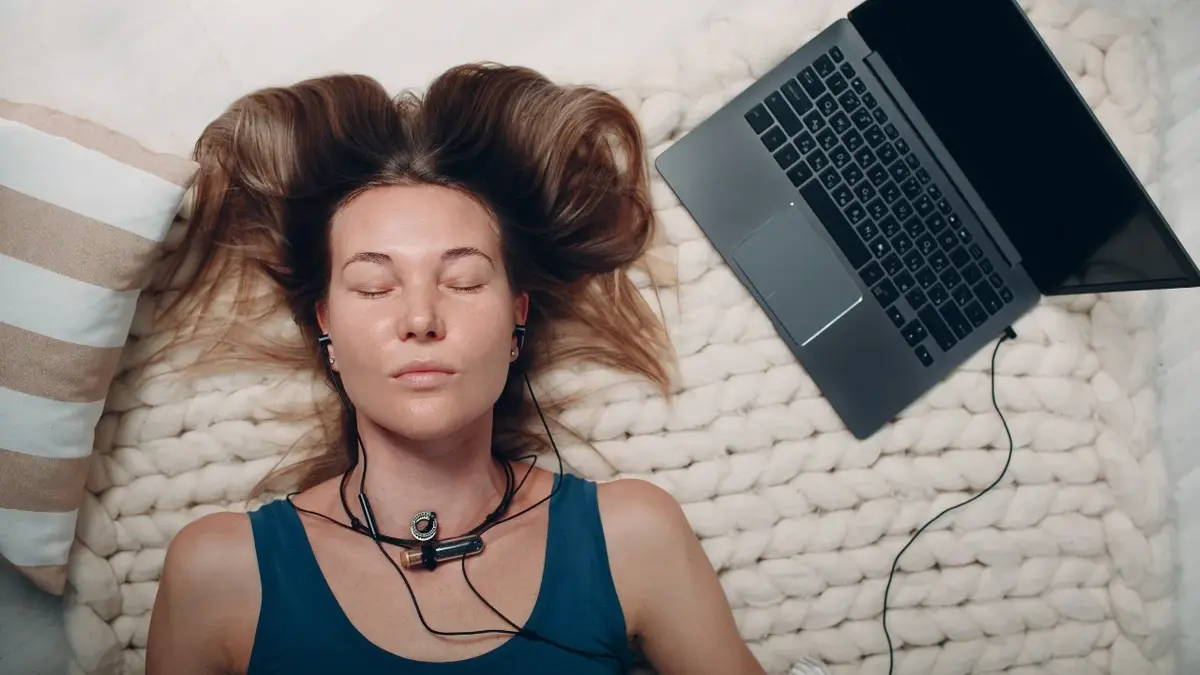 Kobieta leżąca na macie podczas praktyki jogi nidry, obok komputer